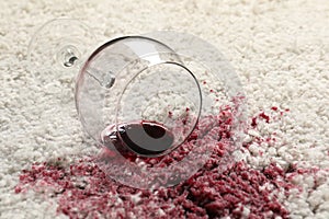 Overturned glass and spilled red wine on white carpet, closeup