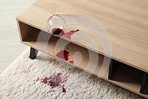 Overturned glass and spilled red wine on white carpet indoors