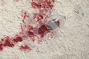 Overturned glass and spilled red wine on white carpet, top view