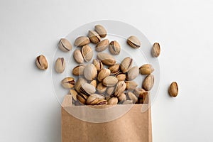 Overturned paper bag with pistachio nuts on white background, flat lay