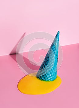 An overturned waffle cone with melted ice cream on a pink background