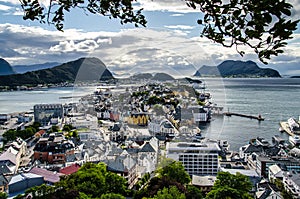 Overview of Alesund town from the Aksla viewpoint during the late evening before sunset with tree leaves framing