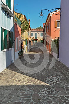 Overview of colorful terraced houses, lamp and bushes in an alley in Burano.