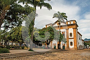 Overview of old colored church, garden with trees and cobblestone street in Paraty.
