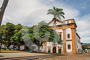 Overview of old colored church, garden with trees and cobblestone street in Paraty.