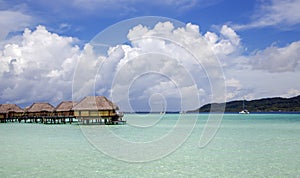 Overwater bungalows stretching out across the lagoon and a few catamarans in a quiet bay in Bora Bora island