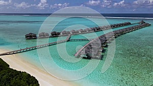 Overwater bungalows at tropical island resort in Maldives. Sunny. Ocean. Sand. Aerial video.