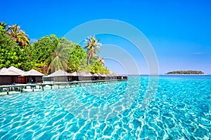 Overwater bungalows on tropical island with sandy beach, palm trees and beautiful lagoon