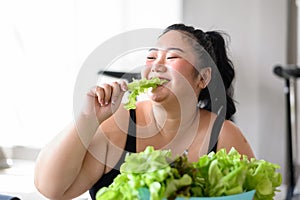 Overweight Asian female happy to eat organic green vegetable salad for healthy in gym. Weight loss workout, healthy lifestyle