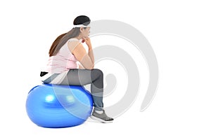 Overweight Asian woman sitting on a gym ball looking bored isolated on white background