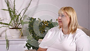 Overweight blonde woman sitting on sofa watching TV