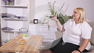 Overweight blonde woman sitting on sofa watching TV