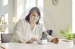 Overweight brunette woman measuring pressure while sitting at table at home