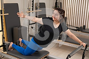 Overweight caucasian woman doing pilates exercises on a reformer.