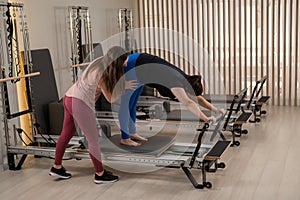 Overweight caucasian woman doing pilates exercises on reformer with personal trainer.