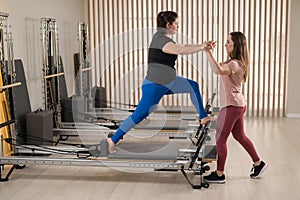 Overweight caucasian woman doing pilates exercises on reformer with personal trainer.