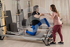 Overweight caucasian woman doing pilates exercises on reformer with personal trainer.