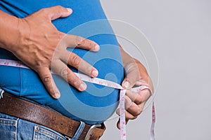 Overweight or fat adult man in very tight jeans with measuring tape on a gray background. Healthcare, medicine concept