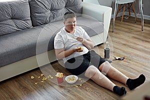 Overweight fat boy eat junk food while watching tv alone at home photo