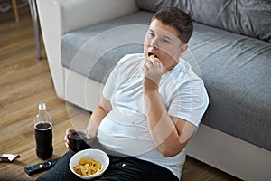 Overweight fat boy eat junk food while watching tv alone at home photo