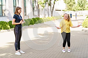Overweight girl jumping with a rope. Her fitness trainer counting reps and looking at a timer.