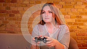 Overweight housewife playing video game using joystick being very attentive and hipped in cozy home.