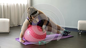 Overweight lady trying to do exercises on fitness ball, making funny attempts