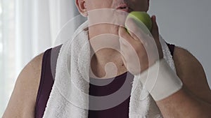Overweight male drinking still water and eating green apple after training, diet
