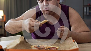 Overweight male eating pizza with delight at night, addiction to unhealthy food