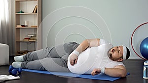 Overweight man breathing heavily after exercises on mat, desire to lose weight