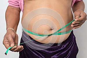 Overweight man check out his body fat with green measuring tape for obesity on gray background, Healthy concept