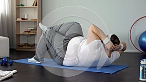 Overweight man doing twisting crunches, pumping abdominal muscles, exercises