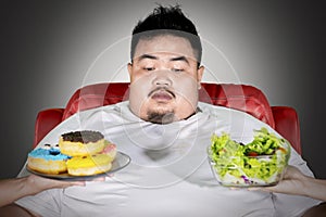 Overweight man doubts to choose donuts or salad