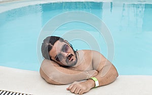 An overweight man dozes off at the side of the swimming pool. Exhausted or bored vacationer