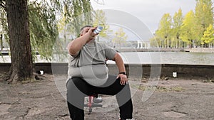 Overweight man drinks water while exercising outdoors. Weight loss concept