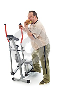 Overweight man eating by an exercising device