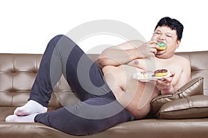 Overweight man eats donuts on sofa