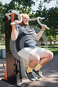 Overweight man exercising on equipment outdoors