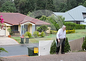 Overweight man having a hard time walking up an extremely steep driveway with neighborhood houses in the background