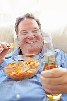 Overweight Man At Home Eating Chips And Drinking Beer