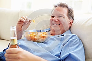 Overweight Man At Home Eating Chips And Drinking Beer