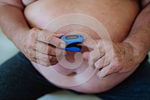 Overweight man iusing a pulse oximeter at home to measure blood oxygen saturation.