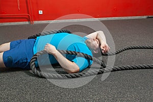 Overweight man is lying on the floor exhausted after performing battle rope exercise in the fitness gym