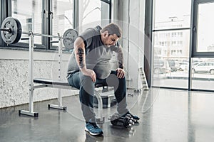 Overweight man sitting on bench after exercising with dumbbells at gym