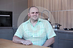 Overweight man sitting at kitchen table and smiles photo