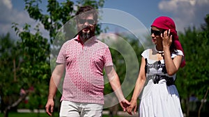 Overweight man and slender woman are walking together in summer day, holding hands and laughing