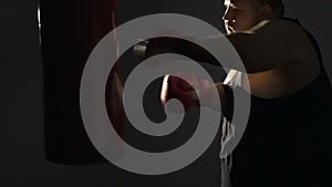 Overweight man striking punching bag, fight with insecurities, slow-motion