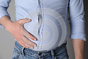 Overweight man in tight shirt on grey background, closeup