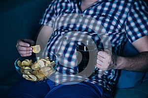 Overweight man watching tv with junk food and beer