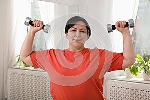 Overweight mature woman doing exercise with dumbbells at home